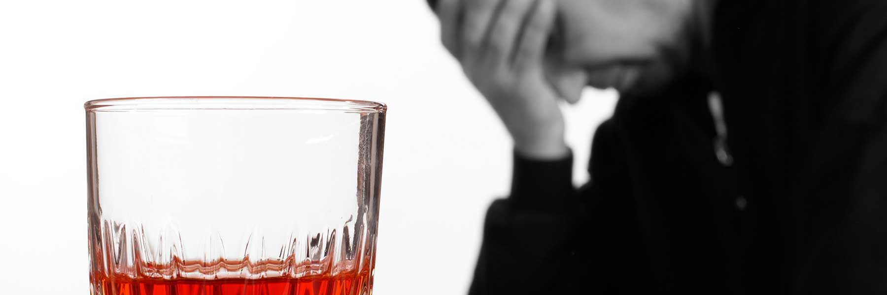 стакан с алкоголем крупным планом на фоне грустного мужчины